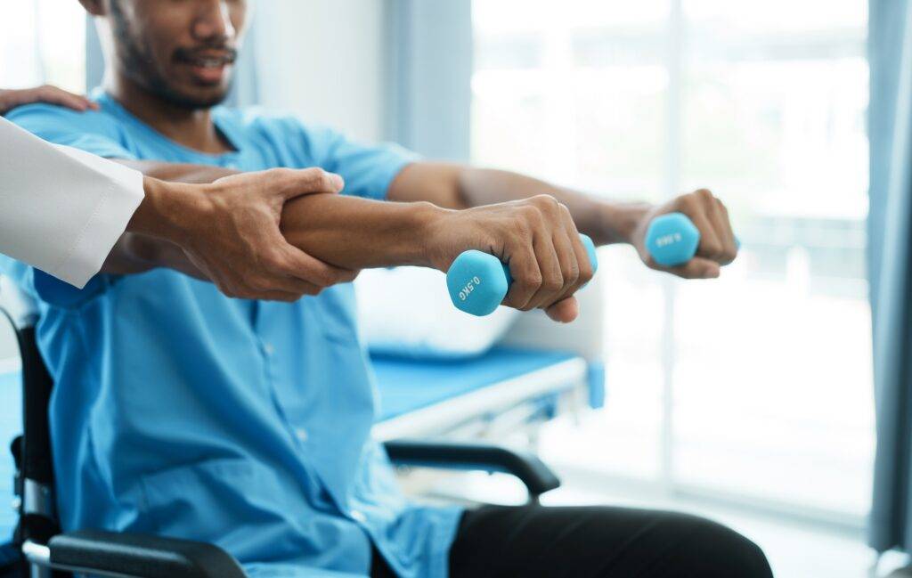 physiotherapist helping male patient in wheelchair exercise with dumbbells.